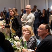 Wide shot of room. Many people in attendance, all giving their attention to speaker